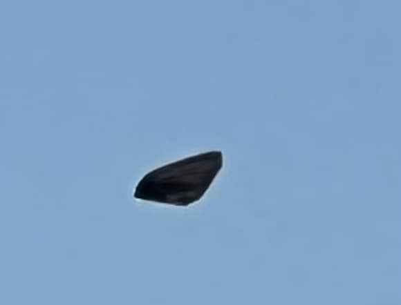 A photograph of a small rounded triangle object floating in a blue sky